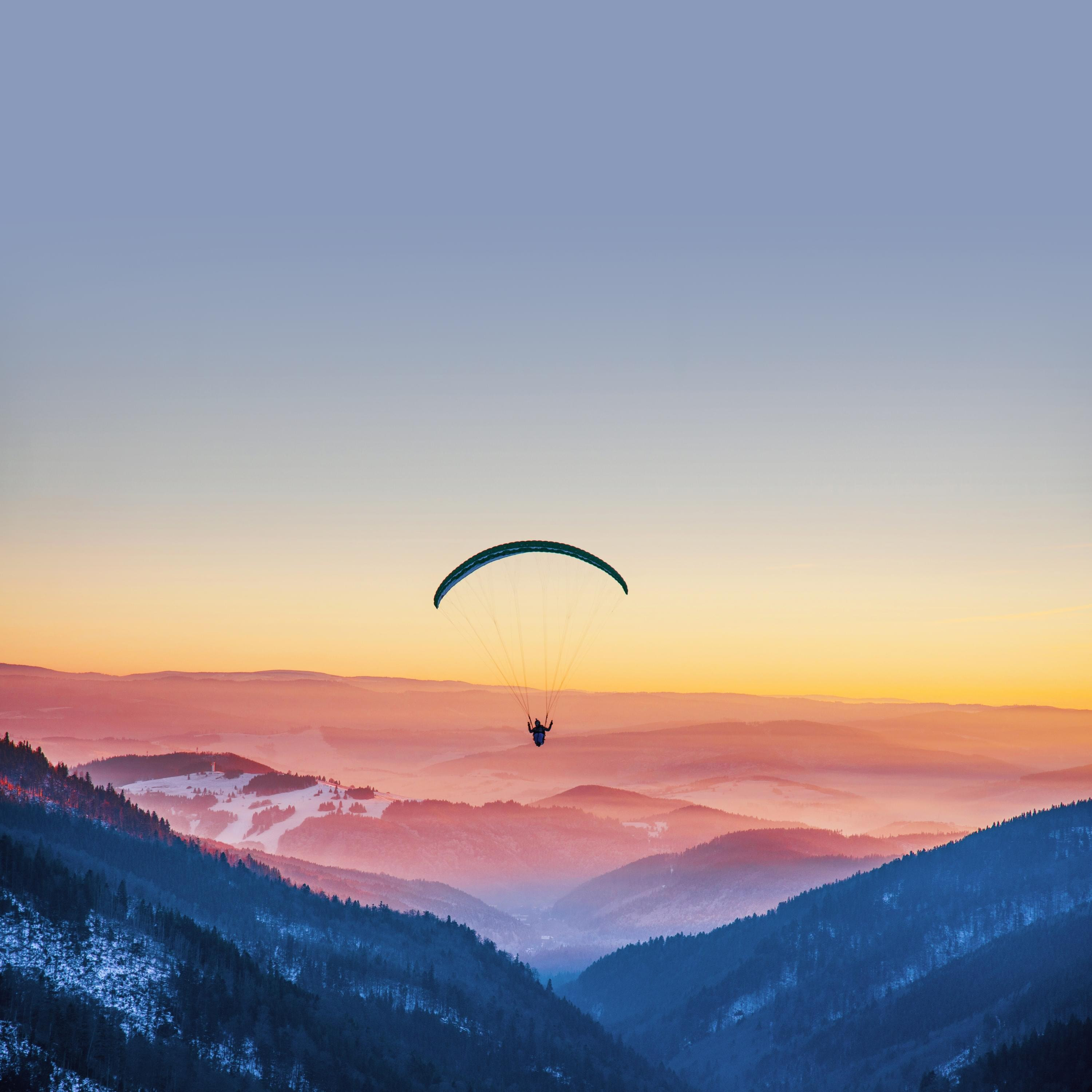 Paraglider soaring above a misty mountain valley at sunset